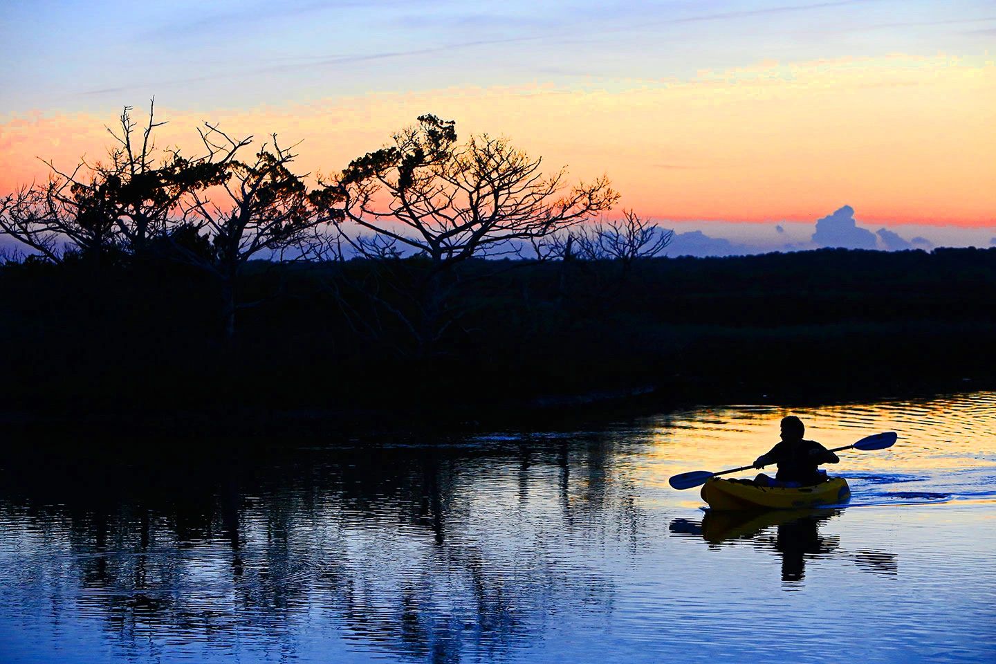 Silhouetted kayaker at sunset on calm water